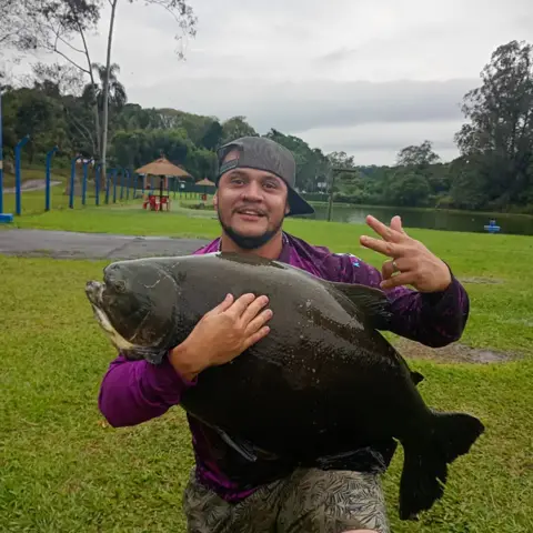Pescador sorrindo com um tambacu enorme nos braços, com o lago ao fundo